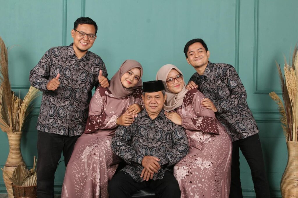 Family portrait featuring adults in coordinating traditional attire against a teal backdrop.