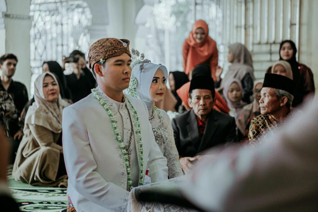 Bride and groom at a traditional Indonesian wedding ceremony with family and friends.