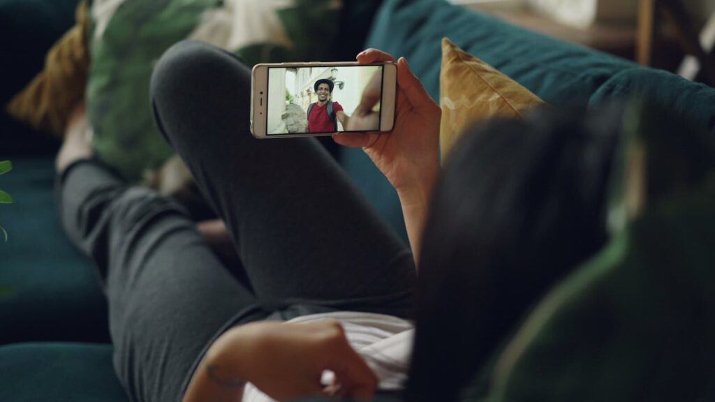 A woman relaxes on a couch while video chatting on her smartphone indoors.
