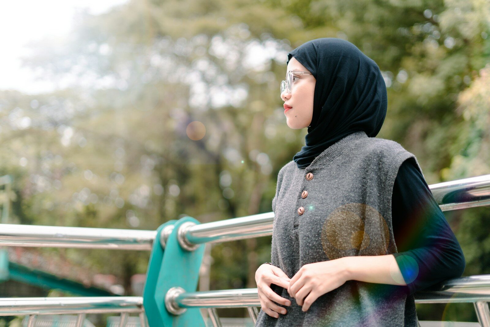 A young woman wearing a hijab and glasses outdoors.