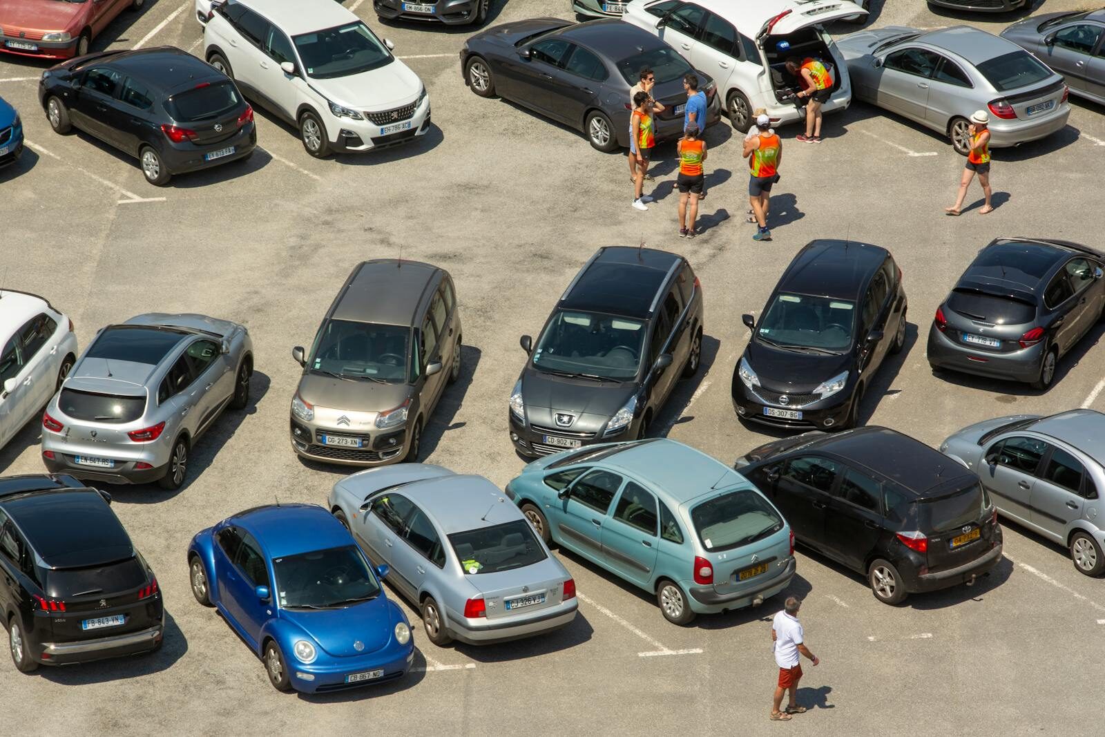 Aerial view of a crowded parking lot with various cars and people congregating.
