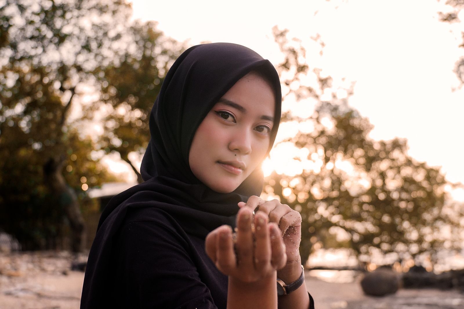 A contemplative woman in a black hijab outdoors at sunset, showcasing serene and cultural beauty.
