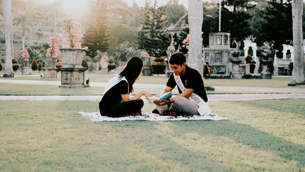 Two people sitting on a blanket in a park